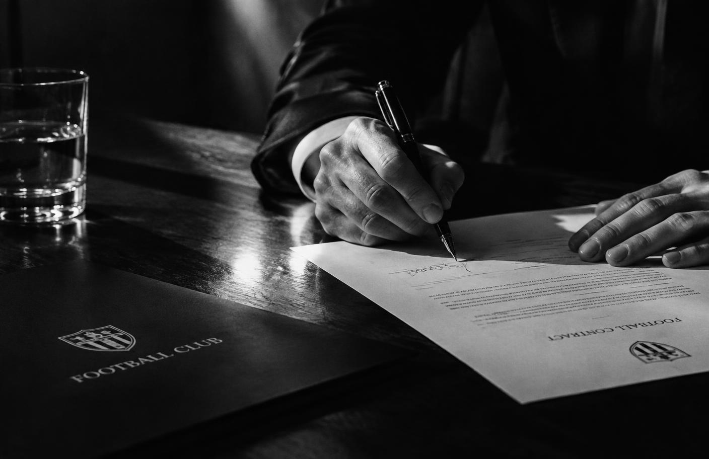 A football contract being signed by fountain pen in dramatic light